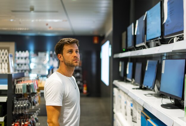 Peinzende man die computer in de winkel kiest