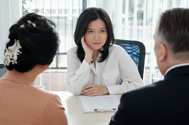 Peinzende mooie jonge zakenvrouw die cv van sollicitant bespreekt met HR-manager en afdelingshoofd tijdens meeting