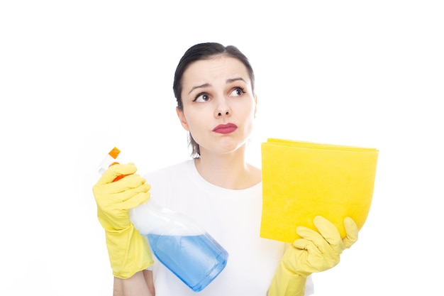 peinzende vrouw in een wit t-shirt op haar handen gele schoonmaakhandschoenen houdt glazenwasser en vodden vast