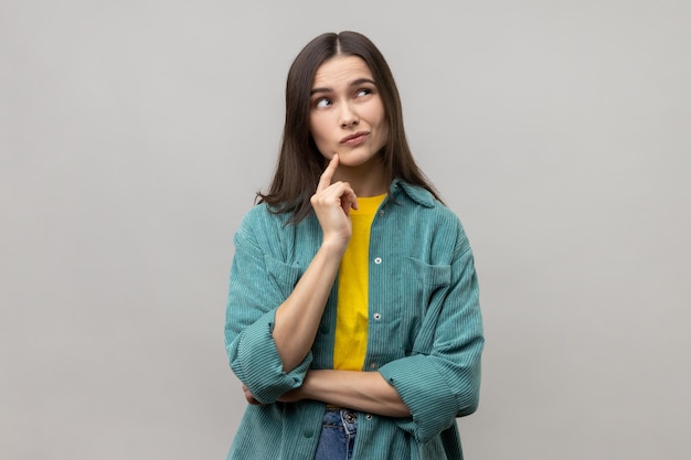 Peinzende vrouw met donker haar die wegkijkt en verwarde gezichtsuitdrukking heeft