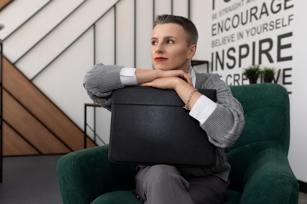 Peinzende zakenvrouw met een leren koffertje in haar handen op kantoor zit in een stoel