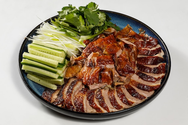 Peking Duck on the plate served with fresh cucumber green onions cilantro and roasted wheaten chinese pancakes with sauce Hoysin on white background