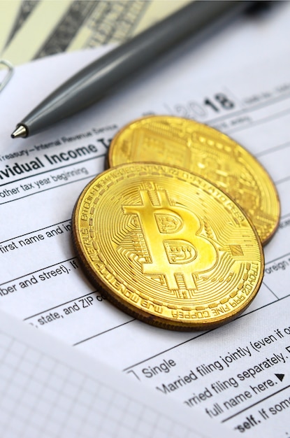 The pen, bitcoins and dollar bills is lies on the tax form 1040