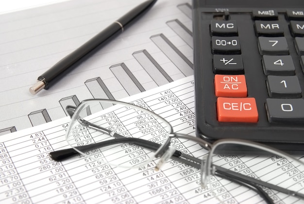 Pen, bril en rekenmachine op papieren tafel met financiële diagram