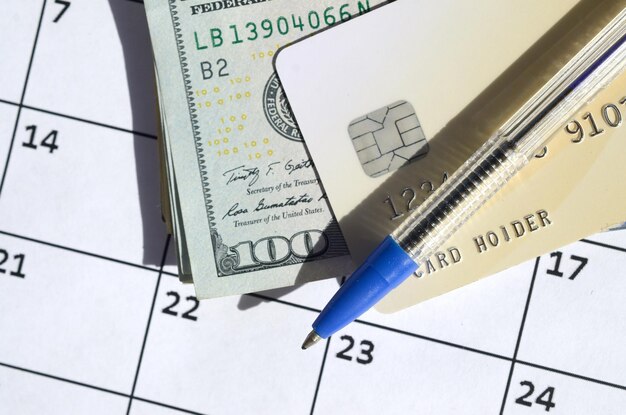 Photo pen and credit card on many hundred us dollar bills on calendar page close up