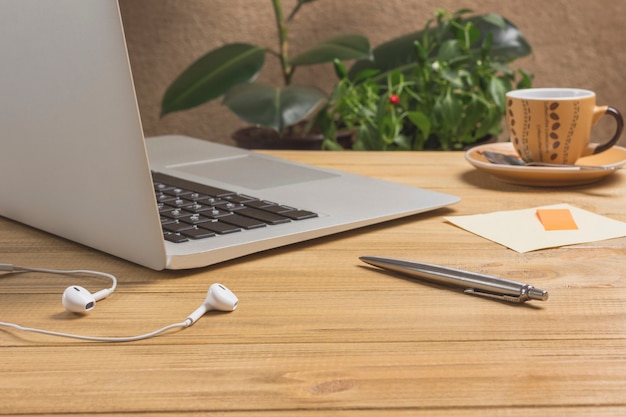 Pen and headphones, laptop, cup of coffee,  on light wood table.