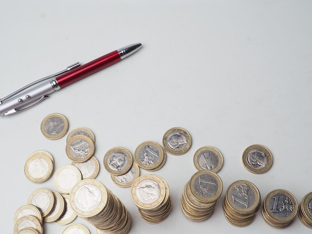 A pen is next to a stack of euro coins.