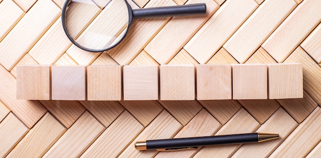 A pen, a magnifying glass and wooden cubes lie on the wooden blocks