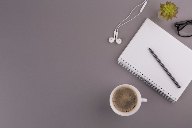 Pen near notepad, cup, earphones and eyeglasses