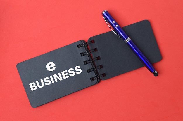 Pen and notebook written with text EBusiness over red background