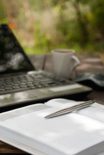 Pen, notitieboekje en laptop op tuinachtergrond.