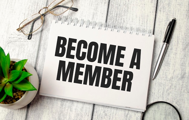 Pen and a white notebook with the text BECOME A MEMBER on wooden background