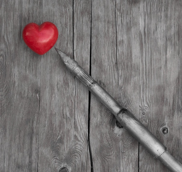 Foto una penna con sopra un cuore rosso è posta su un tavolo di legno.