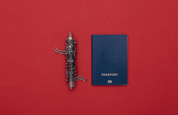 Ручка, обернутая стальной цепью, и паспорт на красном фоне. Вид сверху