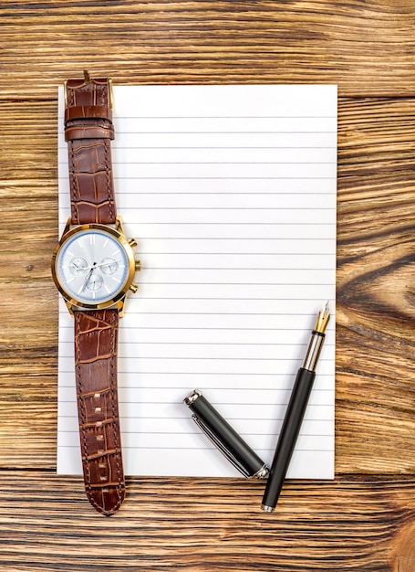 Pen and wrist watch on blank notepad Top view