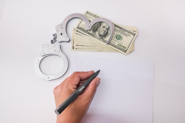 A pen for writing explanations in hand. Arrest, bail, felony, prison. Handcuffs and dollars.