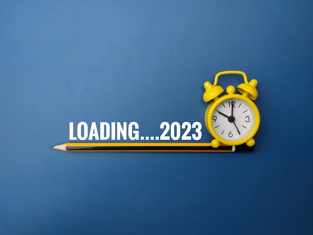 파란색 배경에 LOADING 2023이라는 단어가 있는 연필 및 알람 시계