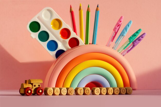 Pencil case in the form of a bright rainbow with a set of school subjects on a pink background. a wooden train with cubes with the inscription Back to school.