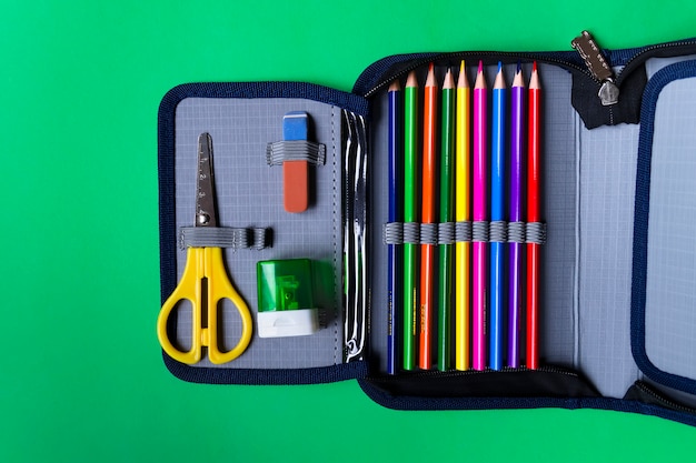 Photo pencil case with school supplies on a green paper background with copy space. flat lay