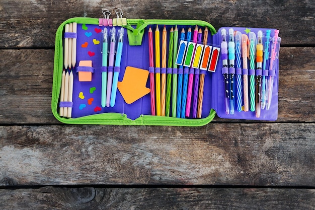 Pencil case with various stationery on old wooden table