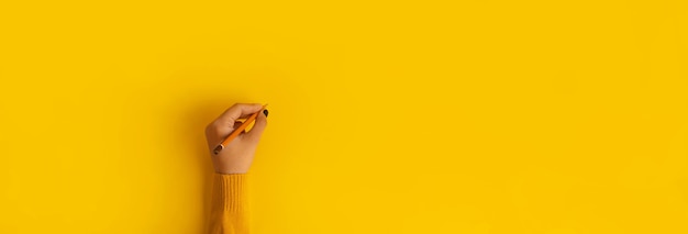 Pencil in hand over yellow background, panoramic mock-up