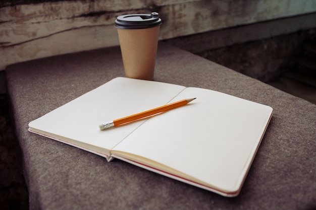 Pencil, notebook and paper coffee cup on a brown fabric background