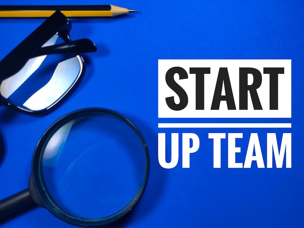pencilglasses and magnifying glass with text START UP TEAM on blue backgroundBusiness concept