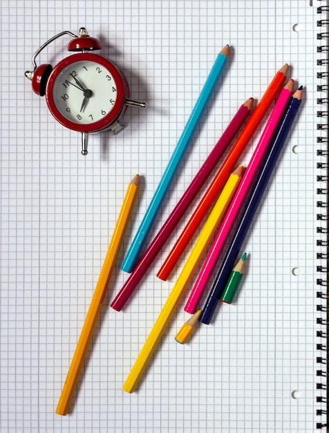 Pencils lying on a notebook and an alarm clock. You can add your text