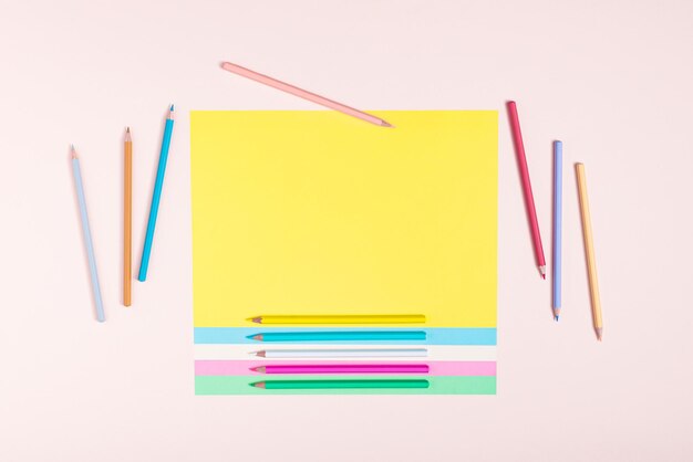 Photo pencils in pastel colors creatively arranged in a pattern on multicolored papers and pink background