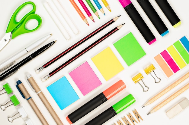 Pencils, pens, stickers, scissors, paper clips, crayons, highlighters, clips and an eraser are laid out using the knolling technique on a light background