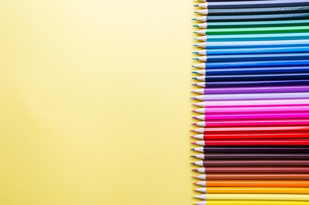 Pencils of various colors on a yellow background, top view with copy space, flat lay