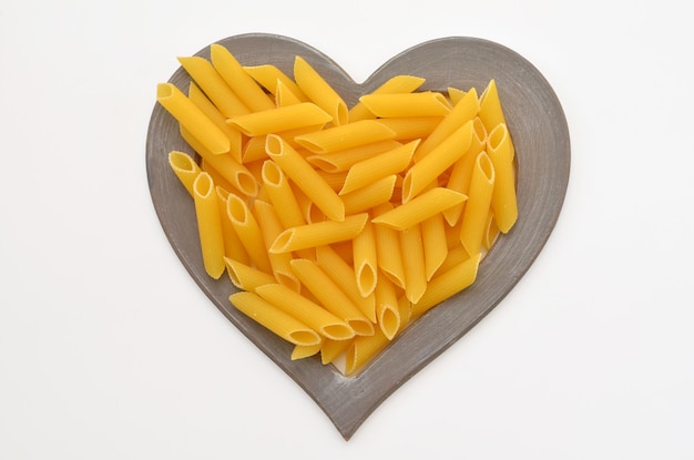 Penne pasta in heart frame on white background