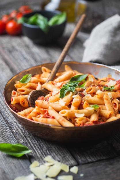 Penne pasta in tomatensaus en kaas versierd met basilicum op een houten