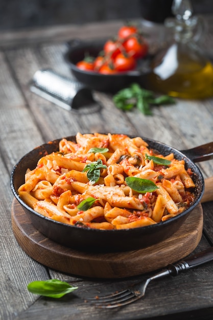 Penne pasta in tomatensaus en kaas versierd met basilicum op een houten