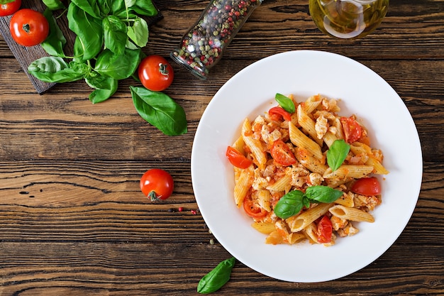 Penne pasta in tomatensaus met kip, tomaten, versierd met basilicum