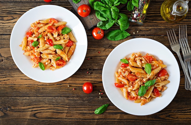 Penne pasta in tomatensaus met kip, tomaten, versierd met basilicum