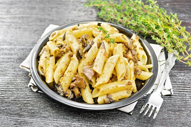 Penne pasta met wilde paddestoelen in een bord op een handdoek, tijm, vork en knoflook op een houten plank achtergrond