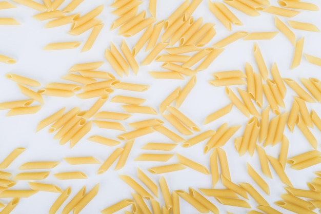 Penne pasta scattered around on top of white background