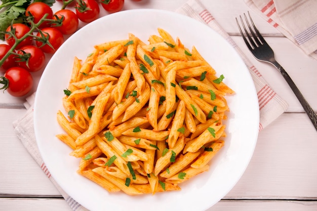 Penne pasta in tomato sauce decorated with parsley on a white wooden table very tasty