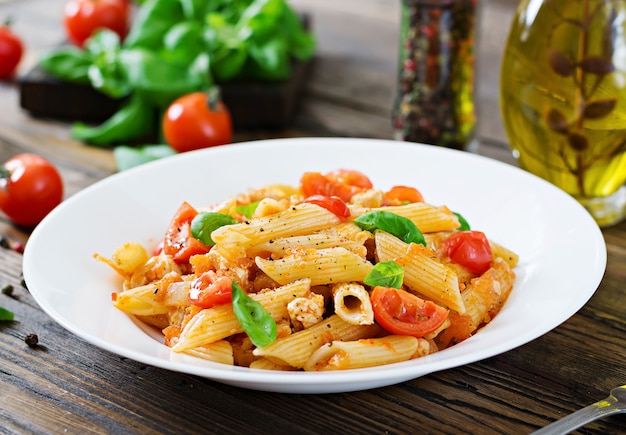 Penne in salsa di pomodoro con pollo, pomodori, decorato con basilico su un tavolo di legno. cibo italiano. pasta al ragù.