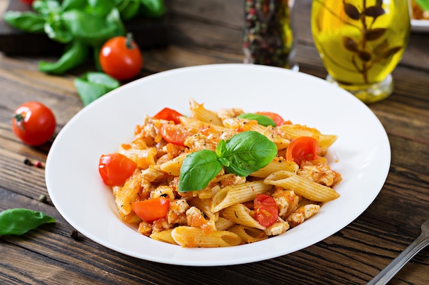 Penne in salsa di pomodoro con pollo, pomodori, decorate con basilico