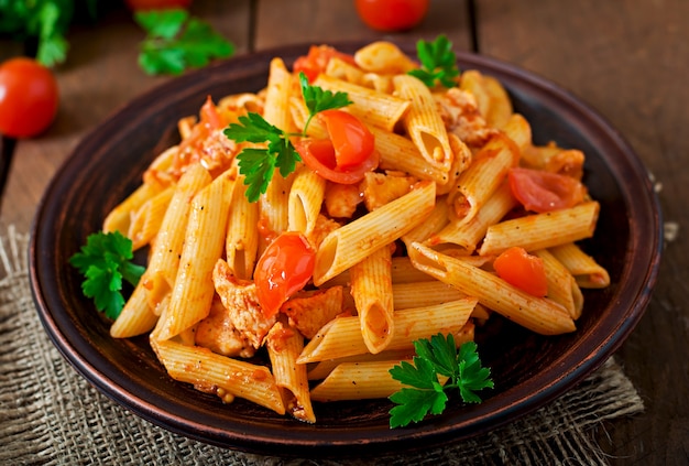 Penne pasta in tomato sauce with chicken and tomatoes on a wooden table