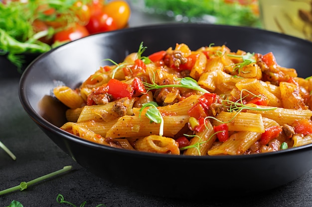 Foto penne in salsa di pomodoro con carne, pomodori decorati con germogli di pisello su un tavolo scuro