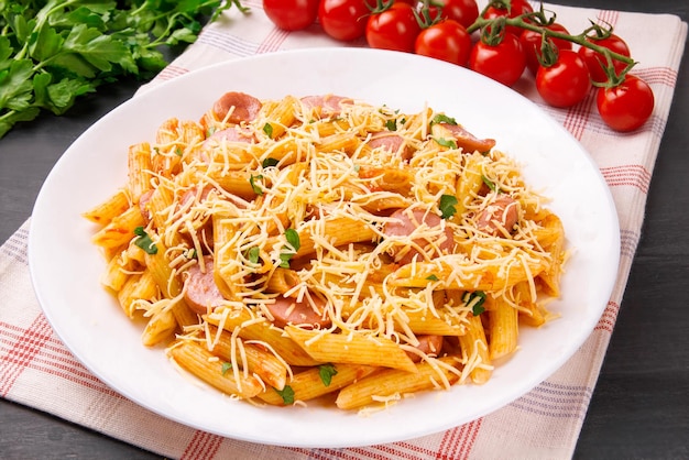 Penne pasta in tomato sauce with sausages and cheese decorated with parsley on a black background very tasty