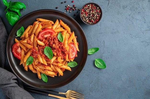 Penne pasta with bolognese sauce on a graphite background. with spices and basil. Italian cuisine.