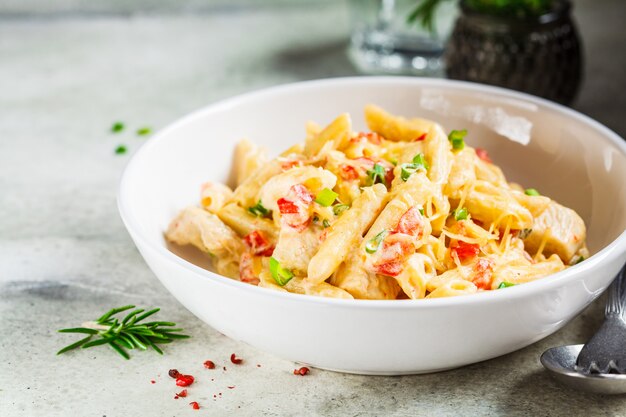 Penne pasta with chicken, pepper and green onions in creamy sauce in a white plate, gray background.