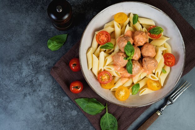 Penne pasta with meatballs tomatoes and sauce on a dark background, top view