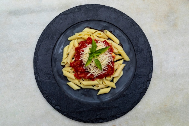 Penne pasta with red sauce and parmesan cheese on a black plate.  Stone or concrete background