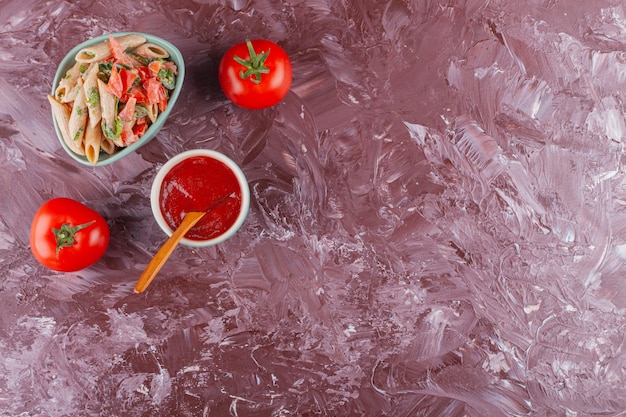 Penne pasta with tomato sauce and fresh red tomatoes on a light table.