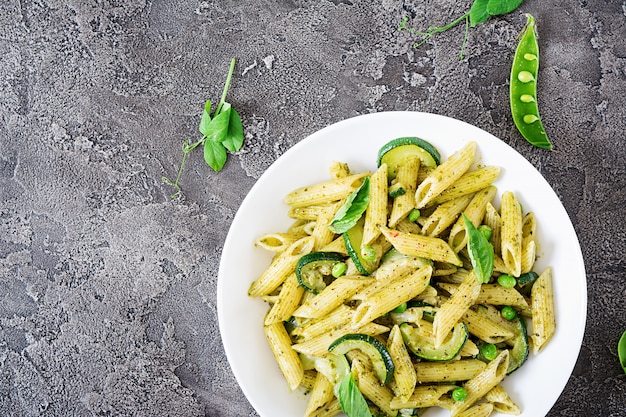 Foto pennedeegwaren met pestosaus, courgette, groene erwten en basilicum. italiaans eten.